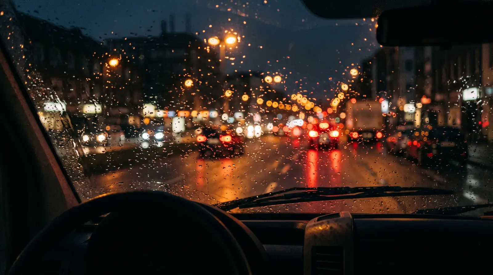 Blick durch die nasse Windschutzscheibe eines Einsatzwagens bei Nacht auf eine Straße im Ruhrgebiet